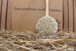 Apaļa pirts birste ar dabīgiem sariem un masāžas lodītēm novietota uz siena fona. Attēlā redzama pirts birste ar garu koka kātu, kas paredzēta ērtai muguras un ķermeņa masāžai.