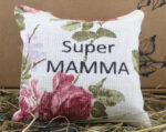 Aromātiskais spilventiņš ar uzrakstu "Super MAMMA" novietots uz siena fona.