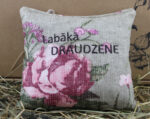 Aromātiskais spilventiņš ar uzrakstu "Labākā DRAUDZENE" novietots uz siena fona.