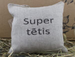 Aromātiskais spilventiņš ar uzrakstu "Super tētis" novietots uz siena fona.