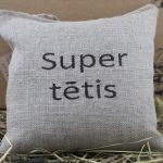 Aromātiskais spilventiņš ar uzrakstu "Super tētis" novietots uz siena fona.