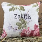 Aromātiskais spilventiņš ar uzrakstu "Zaķītis" novietots uz siena fona.