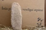 Dabīga lufa pirts dūrainis novietots vertikāli uz siena fona. Attēlā redzams gaišs pirts dūrainis ar rupju tekstūru ķermeņa kopšanai pirtī vai vannā.