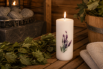 Dekoratīva svece "Lavanda" novietota uz koka lāvas pirts interjerā. Fonā redzama pirts krāsns, pirts slota, koka ķipis un salocīti dvieļi.