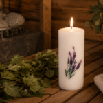 Dekoratīva svece "Lavanda" novietota uz koka lāvas pirts interjerā. Fonā redzama pirts krāsns, pirts slota, koka ķipis un salocīti dvieļi.
