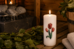 Dekoratīva svece "Tulpes" novietota uz koka lāvas pirts interjerā. Fonā redzama pirts krāsns, pirts slota, koka ķipis un salocīti dvieļi.