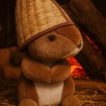 Plīša lācītis ar pirts cepuri, cepure izcelta kā galvenais akcents, novietots uz koka virsmas pirts telpā, silta sauna atmosfēra