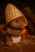 Plīša lācītis ar pirts cepuri, cepure izcelta kā galvenais akcents, novietots uz koka virsmas pirts telpā, silta sauna atmosfēra