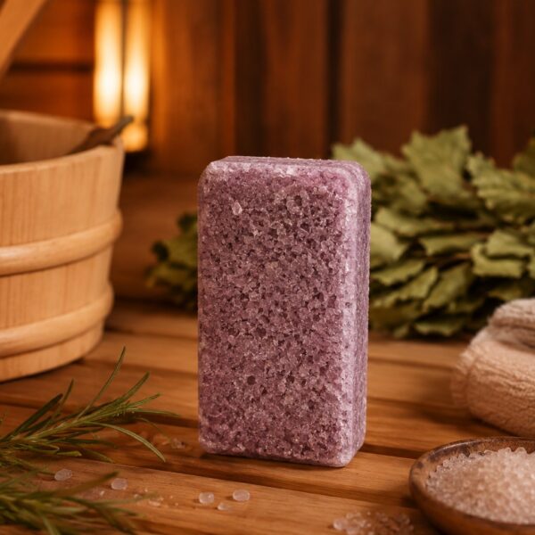 Rozmarīna aromāta sāls bloks novietots siltā pirts atmosfērā uz koka lāvas. Attēlā redzams violetīgs sāls bloks kopā ar rozmarīna zariem, jūras sāls kristāliem, sarullētu dvieli un bērza zariem fonā.