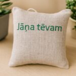 Aromātiskais auduma spilventiņš ar uzrakstu “Jāņa tēvam”, novietots uz gaišas koka virsmas