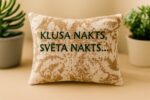 Aromātiskais auduma spilventiņš ar uzrakstu “Klusa nakts, svēta nakts”, novietots uz gaišas koka virsmas