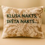 Aromātiskais auduma spilventiņš ar uzrakstu “Klusa nakts, svēta nakts”, novietots uz gaišas koka virsmas
