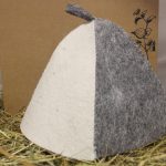Divkrāsu filca pirts cepure baltā un pelēkā krāsā uz siena fona.