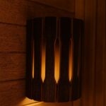 Koka pirts sienas lampa ar aizsargrežģi, uzstādīta pie koka sienas pirts telpā