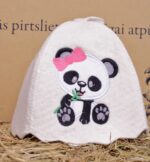 Balta bērnu pirts cepure ar pandas aplikāciju uz salmu fona. Attēlā redzama filca pirts cepure ar melnbaltu pandu un rozā bantīti priekšpusē.
