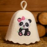 Gaiša filca bērnu pirts cepure ar pandas aplikāciju un rozā bantīti, novietota uz salmiem pirts interjerā