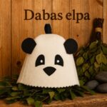 Gaiša filca bērnu pirts cepure ar lielu pandas sejas aplikāciju priekšpusē, novietota uz zaļām bērzu lapām koka pirts interjerā