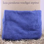 Salocīts zils pirts dvielis novietots uz siena fona. Attēlā redzams mīksts pirts dvielis ar pūkainu tekstūru un piesātinātu zilu krāsu.