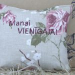 Aromātiskais spilventiņš ar uzrakstu "Manai vienīgajai" un rozā ziedu rakstu novietots uz siena fona. Attēlā redzams dekoratīvs kvadrātveida spilventiņš gaišos toņos.