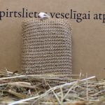 Dabīga lufas pirts švammīte taisnstūra formā novietota vertikāli uz siena fona. Attēlā redzama švammītes priekšpuse ar izteiktu dabīgās lufas tekstūru un baltu cilpiņu augšpusē.