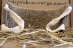 Dabīga lufa pirts dūrainis novietots uz siena fona. Attēlā redzams dūrainis no apakšpuses ar divām gaišām auduma roktura cilpām priekšplānā.