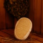Pirts švamme ar elastīgu gumiju rokas uzvilkšanai, novietota uz koka sola pirts telpā