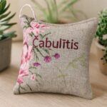 Aromātiskais auduma spilventiņš ar uzrakstu “Čabulītis”, novietots uz gaišas koka virsmas