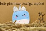 Zila bērnu vannas švammīte vienradža formā novietota uz salmiem dekoratīva fona priekšplānā. Attēlā izcelta švammītes priekšpuse ar sudrabainu ragu, ausīm un izšūtām sejas detaļām.