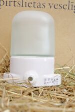 Balta pirts griestu lampa uz salmu fona. Attēlā redzama lampa vertikālā novietojumā ar matētu stikla kupolu un elektrības pieslēguma izvadu korpusa apakšdaļā.