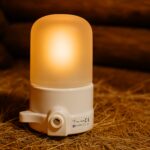 Balta pirts lampa ar matētu kupolu, novietota uz salmiem koka pirts interjerā