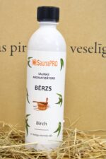 SaunaPRO saunas aromatizētājs "Bērzs" uz salmu fona. Attēlā redzama balta plastmasas pudele ar bērza motīvu etiķeti un melnu skrūvējamu vāciņu.