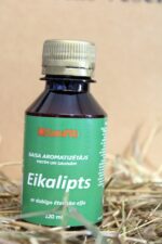 Gaisa aromatizētājs pirtīm un saunām "Eikalipts" uz salmu fona. Attēlā redzama tumša plastmasas pudele ar zaļgani zilu etiķeti un metālisku skrūvējamu vāciņu.