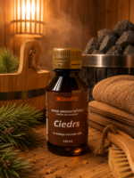 Gaisa aromatizētājs pirtīm ar ciedra aromātu 120 ml tumšā stikla pudelē novietots uz koka galda pirts interjerā. Blakus redzams koka pirts spainis, pirts krāsns akmeņi, salocīti dvieļi un skuju zari.