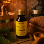 Gaisa aromatizētājs pirtīm ar citrona aromātu 120 ml tumšā stikla pudelē novietots uz koka galda pirts interjerā. Blakus redzams koka pirts spainis, pirts krāsns akmeņi, salocīti dvieļi un egļu zari.