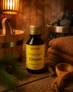 Gaisa aromatizētājs pirtīm ar citrona aromātu 120 ml tumšā stikla pudelē novietots uz koka galda pirts interjerā. Blakus redzams koka pirts spainis, pirts krāsns akmeņi, salocīti dvieļi un egļu zari.