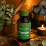 Gaisa aromatizētājs pirtīm ar eikalipta aromātu 120 ml tumšā stikla pudelē novietots uz koka galda pirts interjerā. Blakus redzams koka pirts spainis ar kausiņu, eikalipta zari un aizdegta svece.