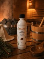 Pirts aromatizators ar darvas aromātu 500 ml baltā pudelē novietots uz koka lāvas pirts interjerā. Fonā redzama pirts krāsns ar akmeņiem, koka spainis un pirts cepure.