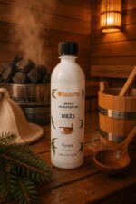 Pirts aromatizators ar meža aromātu 500 ml baltā pudelē novietots uz koka lāvas pirts interjerā. Fonā redzama pirts krāsns ar akmeņiem, koka spainis un pirts cepure.