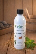 Pirts aromāts “Piparmētra” baltā pudelē, novietots uz koka virsmas blakus svaigām piparmētru lapām