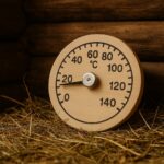 Apaļš koka pirts termometrs temperatūras mērīšanai, novietots uz salmu klājuma pirts vidē