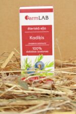FarmLAB kadiķa ēteriskā eļļa iepakojumā novietota uz salmiem, redzams produkta iepakojums ar kadiķa ogu un zaru attēlu