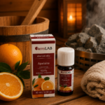 Ēteriskā eļļa Apelsīns 10 ml pudelītē ar iepakojumu novietota uz koka lāvas pirts interjerā. Blakus redzams svaigs apelsīns, fonā – koka spainis, dvielis un pirts krāsns.
