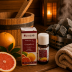 Ēteriskā eļļa Greipfrūts 10 ml pudelītē ar iepakojumu novietota uz koka lāvas pirts interjerā. Blakus redzams greipfrūts, fonā – koka spainis, dvielis un pirts krāsns.