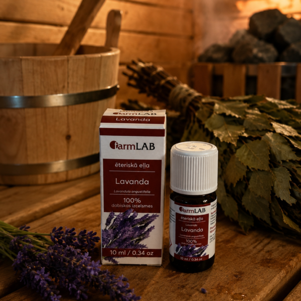 Ēteriskā eļļa Lavanda 10 ml pudelītē ar iepakojumu novietota uz koka lāvas pirts interjerā. Fonā redzama pirts slota, koka spainis un lavandas ziedi.