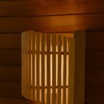 Koka pirts sienas lampa ar vertikālu aizsargrežģi, uzstādīta pie koka sienas pirts telpā