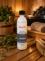 Pirts lāvu mazgāšanas līdzeklis ar kadiķa aromātu 500 ml baltā pudelē novietots uz koka lāvas pirts interjerā. Blakus redzami kadiķa zari, koka pirts spainis, pirts krāsns akmeņi un pirts birste.