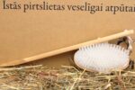 Garā koka pirts masāžas birste ar baltiem sariem novietota uz salmu klājuma gaišā fonā