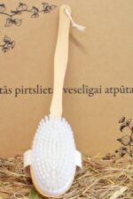 Garā koka pirts masāžas birste ar baltiem sariem novietota vertikāli uz salmu klājuma gaišā fonā