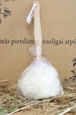 Mazgāšanās sūklis ar koka rokturi caurspīdīgā iepakojumā, novietots uz salmu klājuma