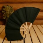Tumši zaļš pirts vēdeklis ar koka karkasu, novietots uz koka lāvas